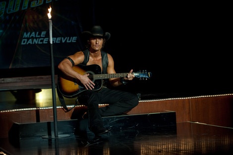 a man with a cowboy hat playing an acoustic guitar in front of a microphone on stage