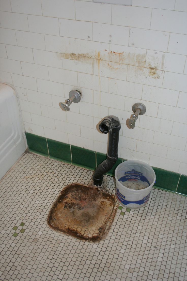 a dirty bathroom with a drain in the floor and a bucket on the ground next to it