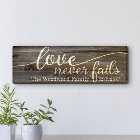 a wooden sign with the words love never falls on it next to two potted plants