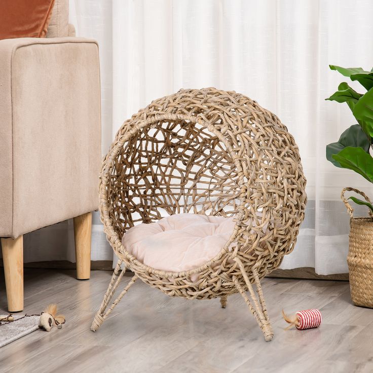 a cat is sitting in a wicker ball chair on the floor next to a potted plant