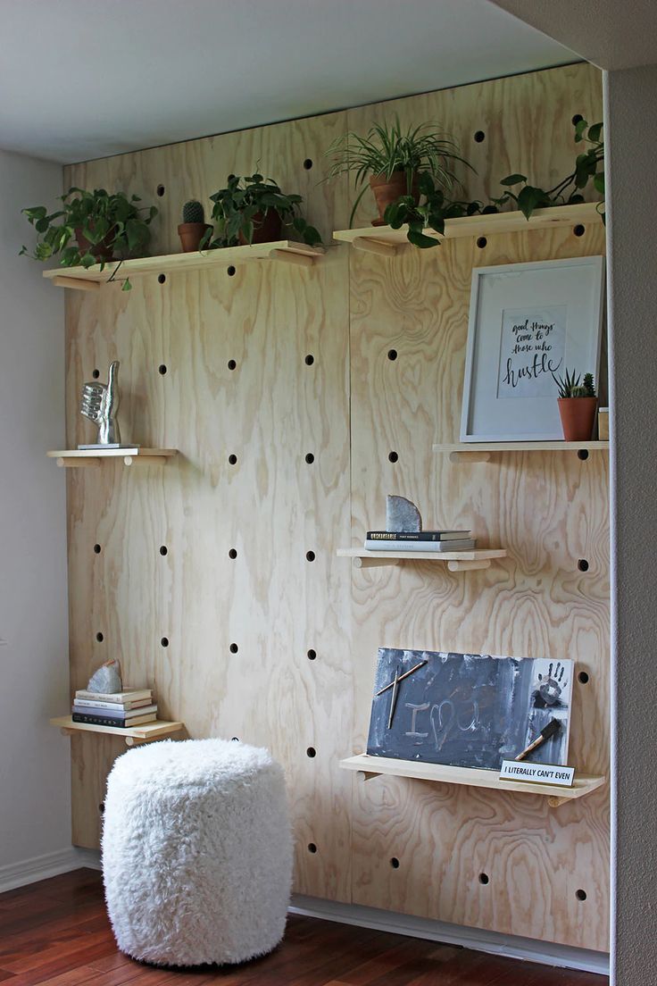 a room with some shelves and plants on the wall, along with a pouffle ottoman