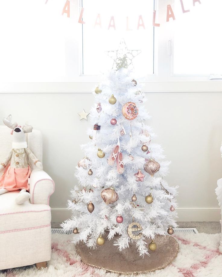 a white christmas tree in a room with pink and gold ornaments on the top, sitting next to a chair