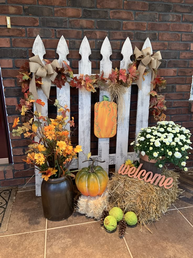 pumpkins, hay bales and flowers sit in front of a white picket fence