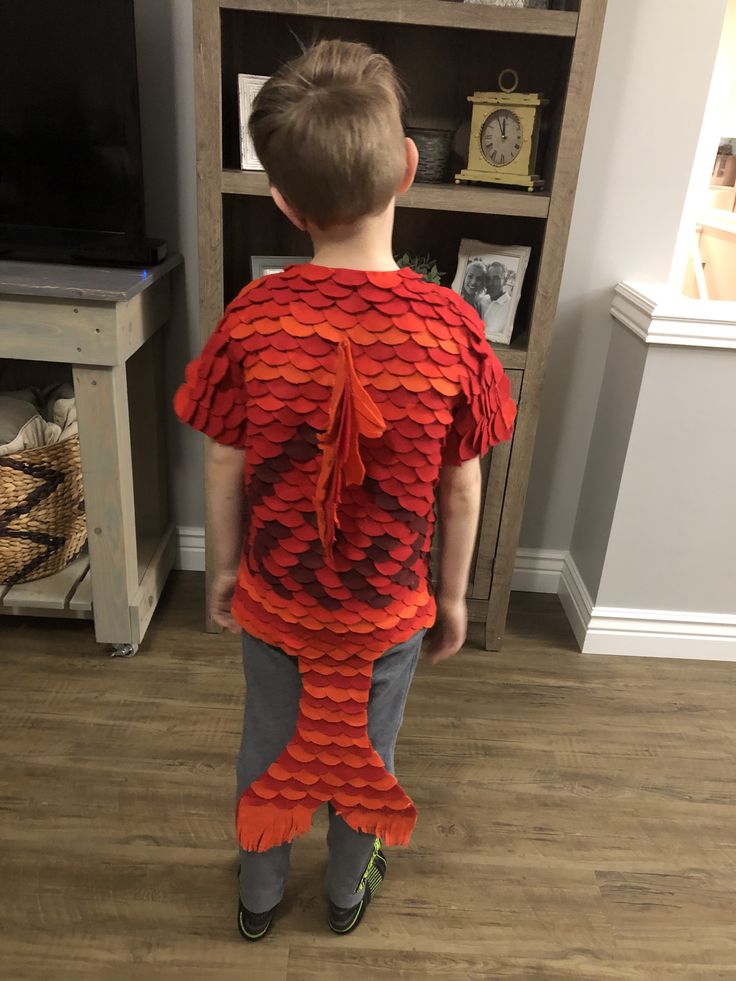 a young boy standing in front of a bookshelf wearing an orange fish costume