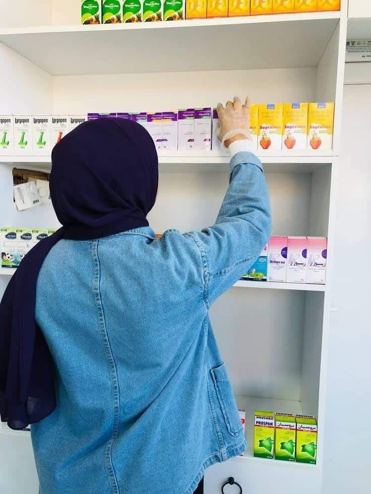 a woman in a hijab is picking up some medicine from the pharmacy shelf