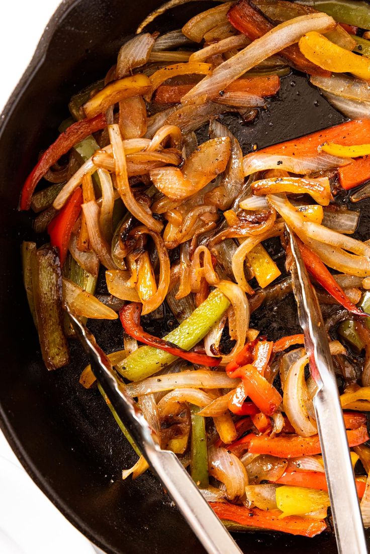 stir fry vegetables being cooked in a wok with tongs and seasonings on the side