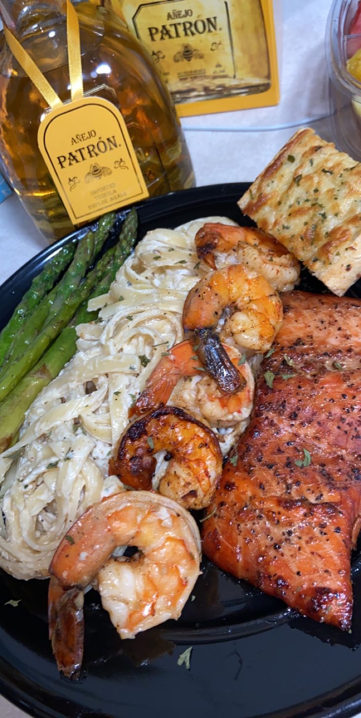 a black plate topped with shrimp, pasta and asparagus next to wine bottles