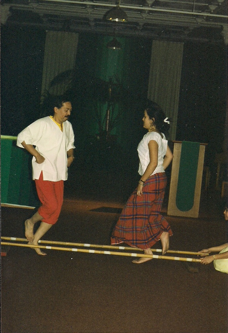 two people are walking on the floor in front of a curtained area and one person is wearing a white shirt and red pants