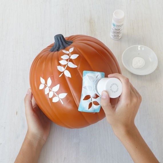 someone is painting a pumpkin with white paint on the top and bottom part, along with other items to decorate it