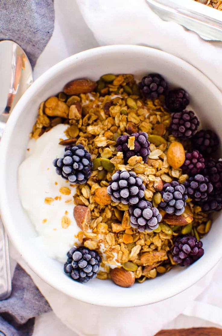 a bowl filled with granola and fruit on top of a white cloth next to silverware