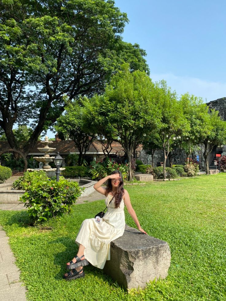 a woman sitting on top of a stone bench in a grassy area next to trees