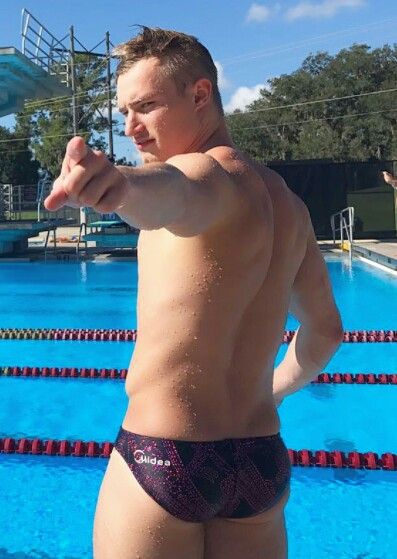 a man with no shirt standing in front of a swimming pool pointing at the camera