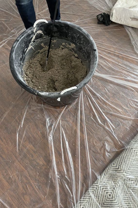 a person standing on top of a wooden floor covered in plastic covering the floor with a bucket