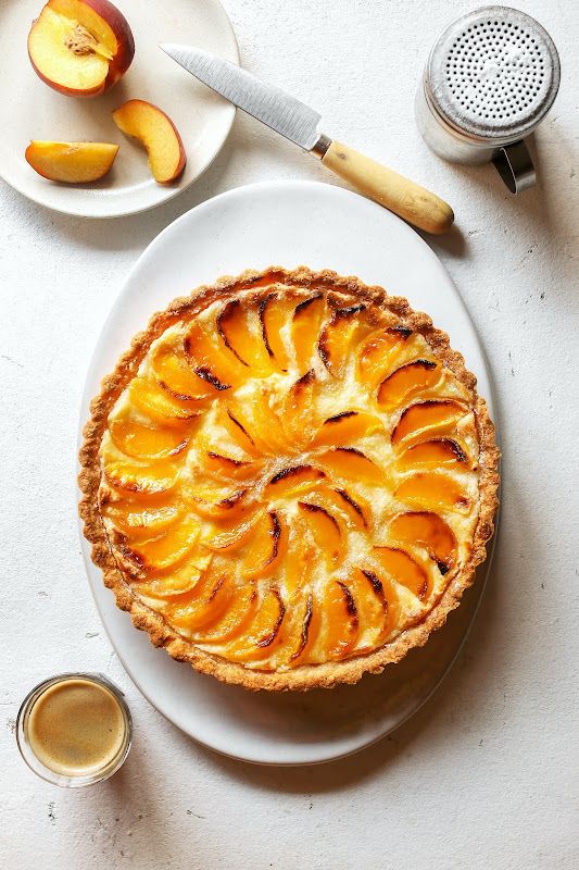 a peach pie on a plate next to some sliced peaches