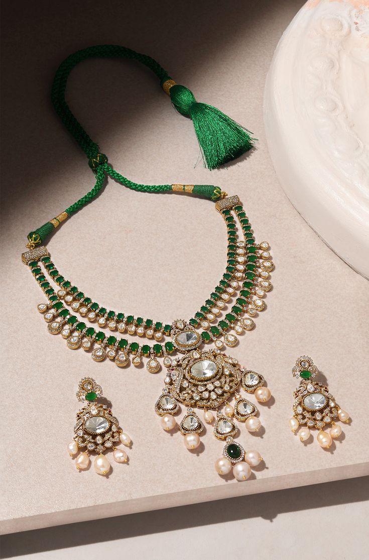 Unveil timeless elegance with this Layered Green Pendant Necklace Set, crafted with precision and style. The set is made from durable brass with a lustrous yellow gold finish, featuring a cascade of layers that exude sophistication. At its heart is a striking green emerald pendant, framed by sparkling Polki stones for an added touch of glamour. Delicate pearls are interspersed throughout, lending a classic, refined feel to the design. The vibrant green hues are balanced by the warm gold and the Opulent Hand Set Necklace For Gift, Elegant Gold Kundan Necklace Made Of Brass, Elegant Gold Kundan Necklace In Brass, Opulent Gold Jewelry With Elegant Design, Elegant Brass Jewelry Sets For Celebration, Elegant Brass Necklaces For Wedding, Elegant Brass Wedding Necklaces, Festive Formal Brass Necklace, Formal Festive Brass Necklace