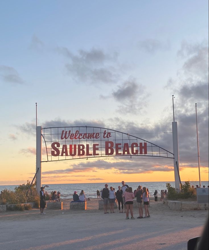 people are standing under the welcome sign for a public beach area at sunset or sunrise