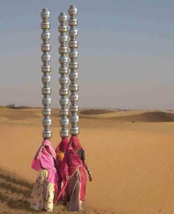 two women are walking in the desert with metal balls on their heads and legs,