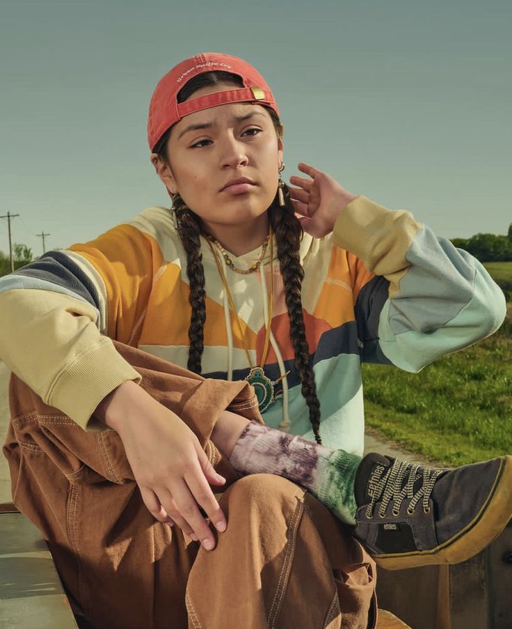 a woman sitting on top of a wooden bench wearing a red hat and braids