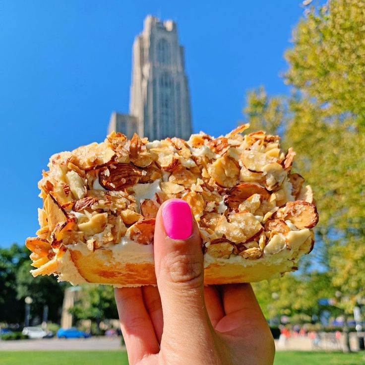 a person holding up a half eaten doughnut in front of a tall building on a sunny day