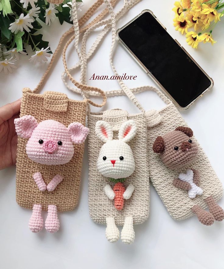 three small crocheted animal purses on a table with flowers and a cell phone