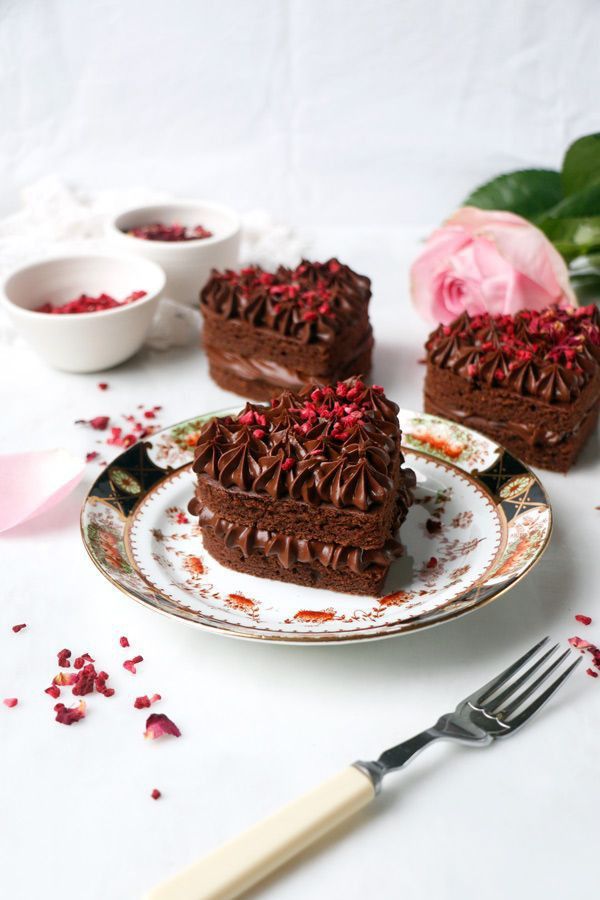 three pieces of heart shaped chocolate cake on a plate next to a fork and rose petals