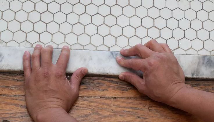 two hands on the edge of a tile floor next to a hand reaching for it