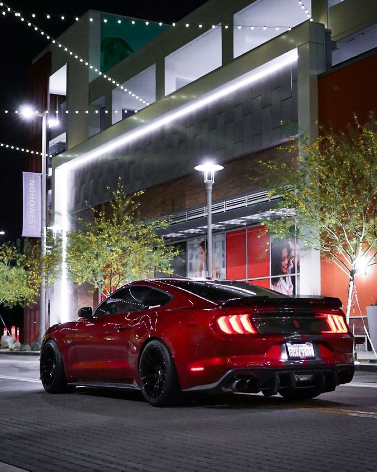 a red sports car is parked in front of a building at night with lights on