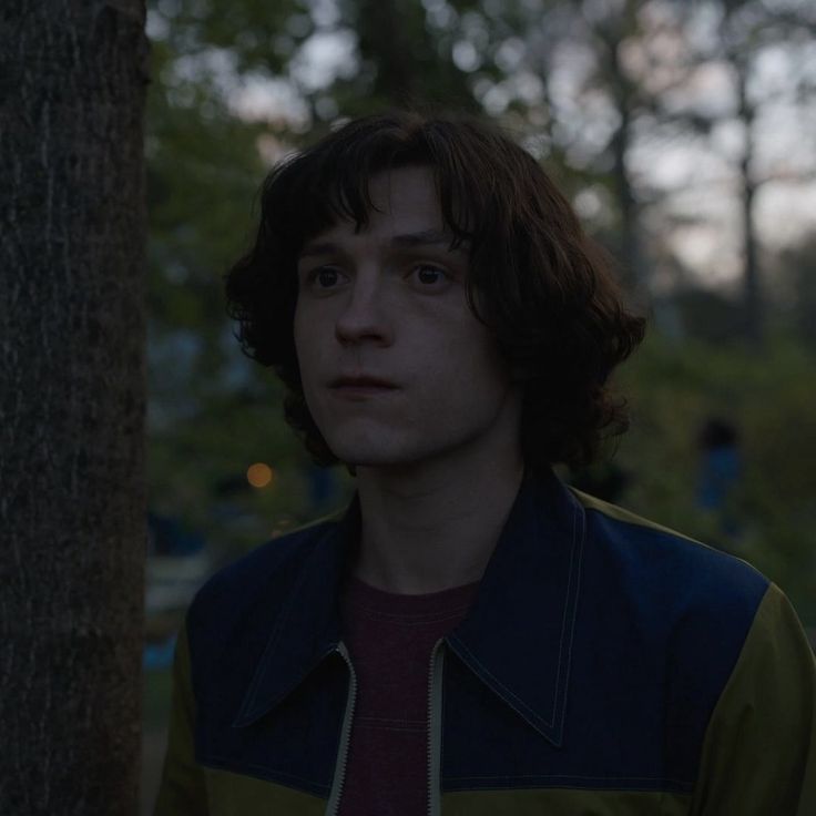 a man standing next to a tree in the woods