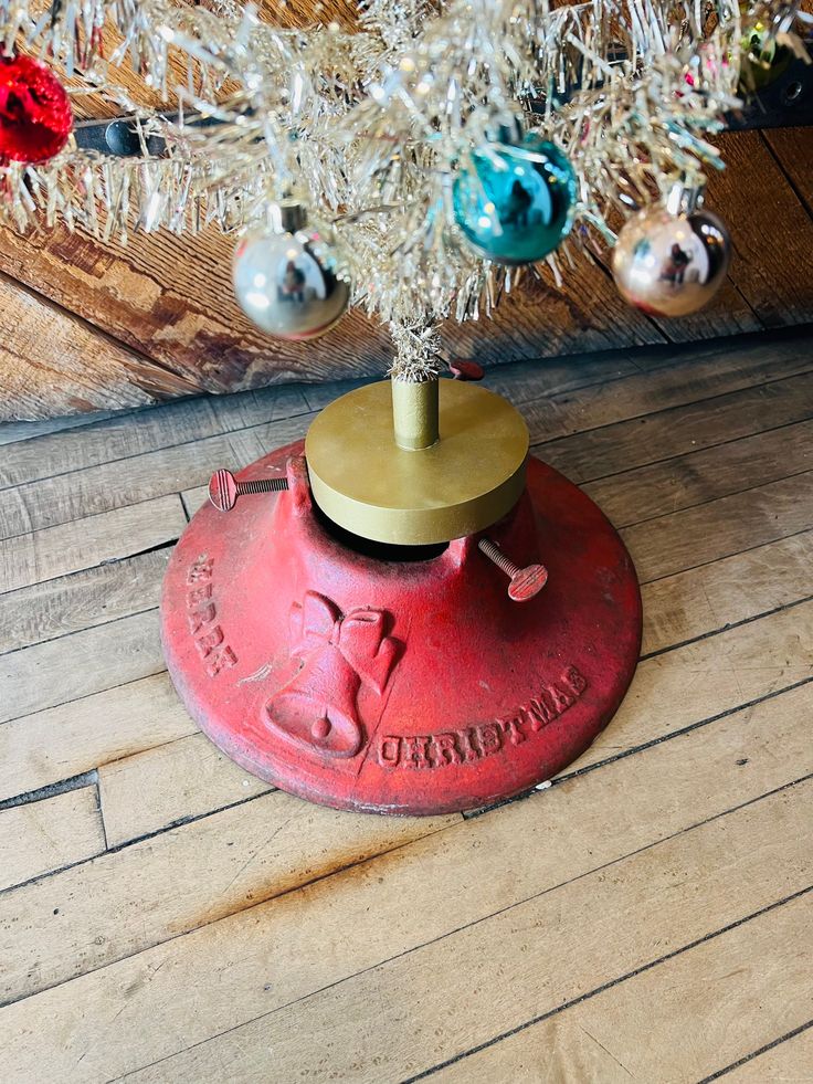 a small christmas tree on top of a red metal base with ornaments hanging from it