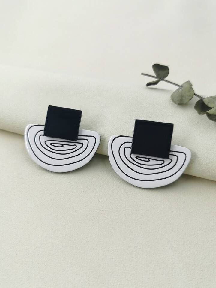 two black and white square shaped earrings sitting on top of a piece of paper next to flowers