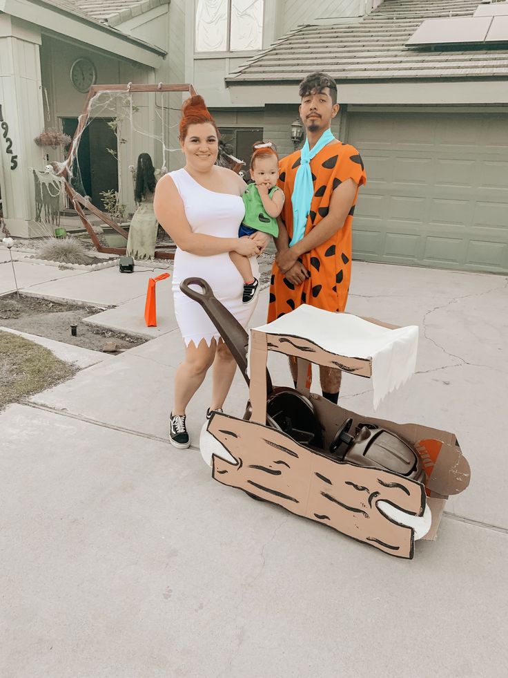 a man and woman are standing in front of a cardboard boat with a child on it