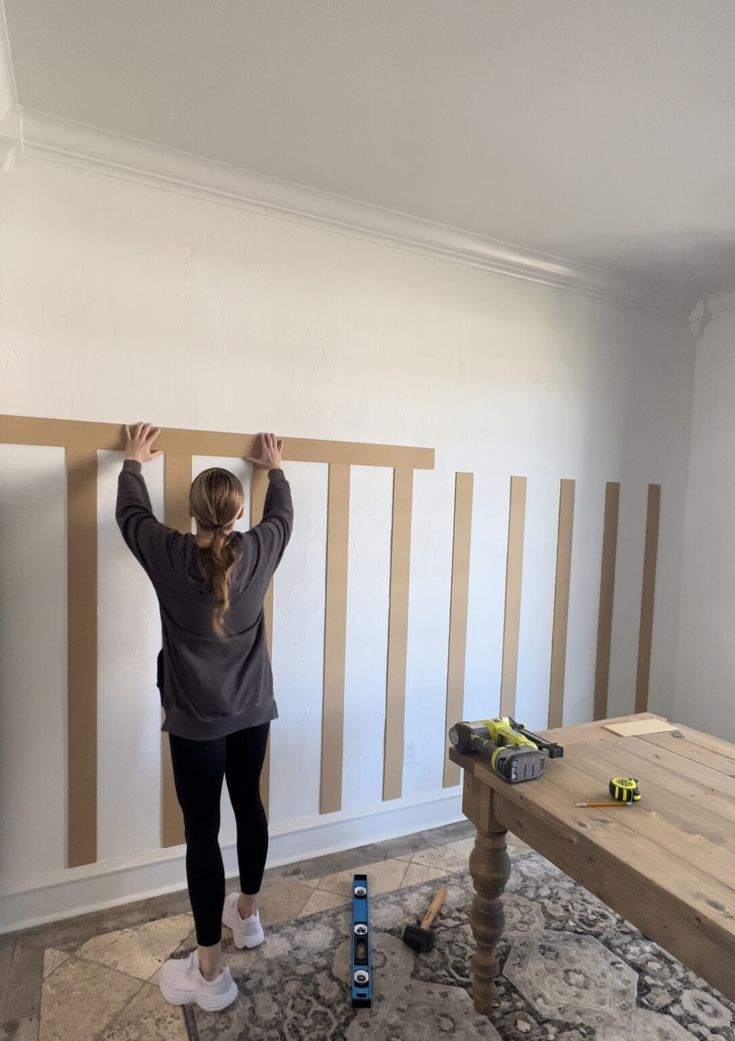 a woman standing in front of a wall with wooden slats on it and her hands up