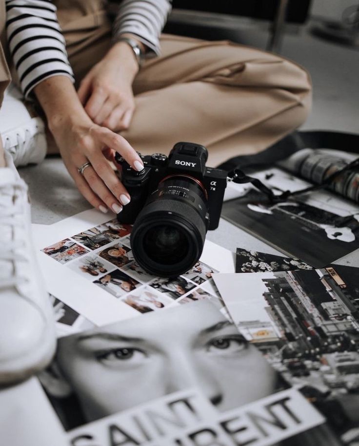 a woman sitting on the floor with a camera in front of her and several photographs surrounding her