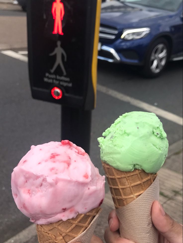 two ice cream cones with green and pink toppings in front of a parking meter