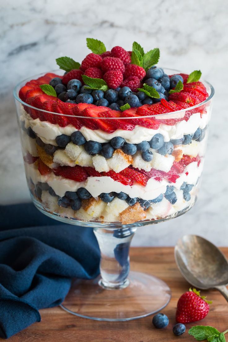 a trifle with berries, bananas and blueberries in a glass dish on a wooden table