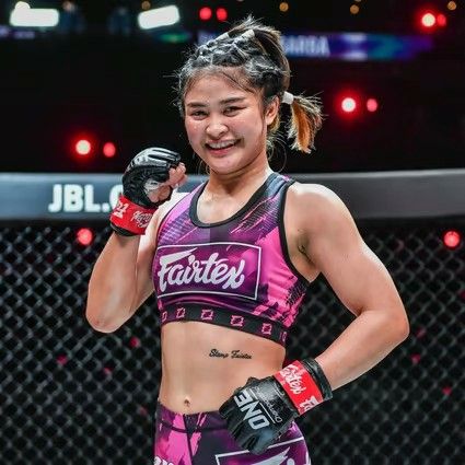 a female fighter posing for the camera with her boxing gloves on and one hand up