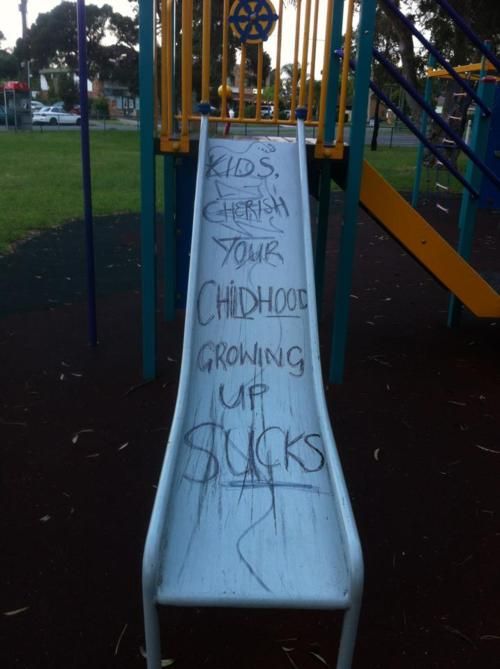 a slide with graffiti written on it in a park area next to a play structure