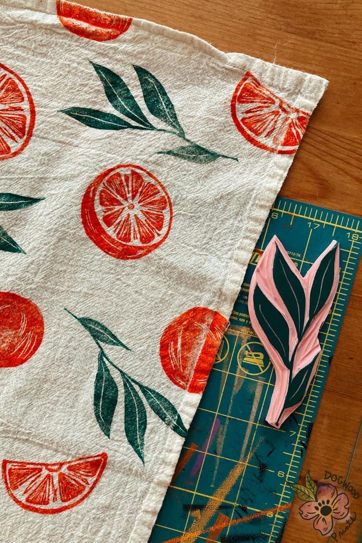 a piece of fabric with oranges and leaves on it next to a cutting board