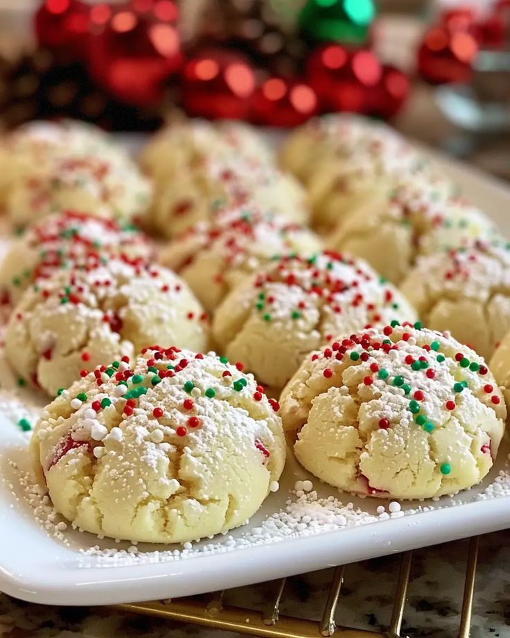 several cookies with sprinkles on a white plate next to a red and green christmas ornament