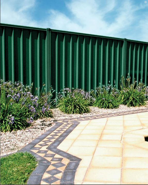 a green metal fence next to some plants