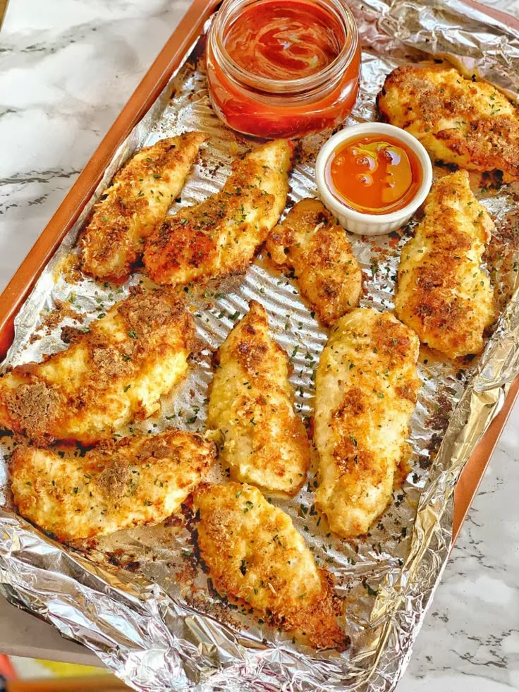 chicken wings on tin foil with ketchup and dipping sauce in the container next to them