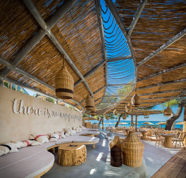 an outdoor seating area with wicker tables and umbrellas on the roof over looking the ocean