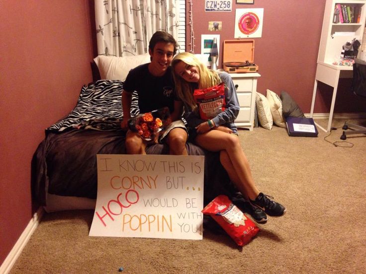 two people sitting on a bed with a sign that says i know this is corny but it would be popcorn with you