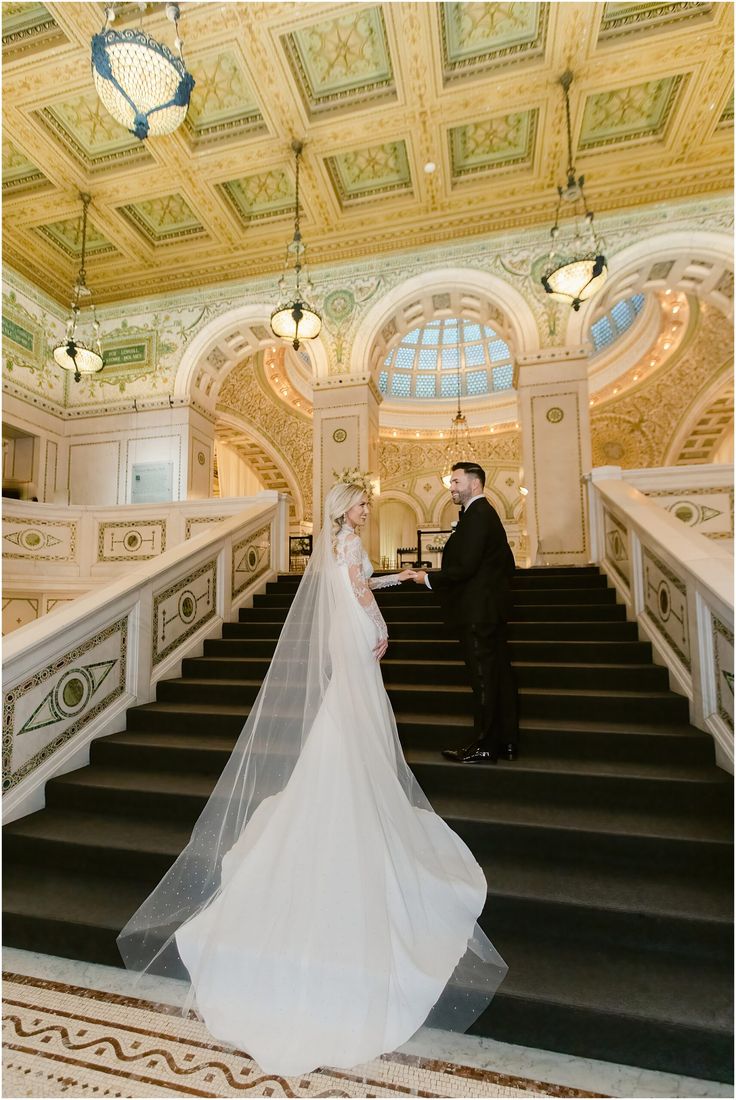 a bride and groom standing on the stairs at their wedding ceremony in an ornate building