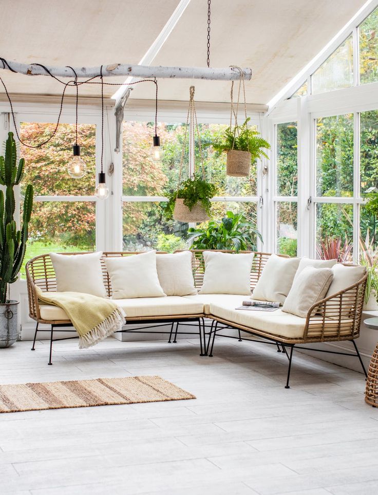 a living room filled with lots of plants next to a large white couch and windows