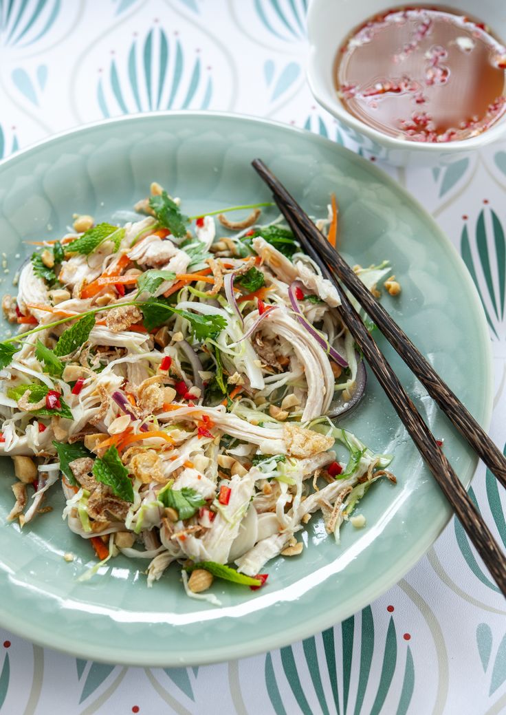 a green plate topped with salad and chopsticks next to a cup of tea