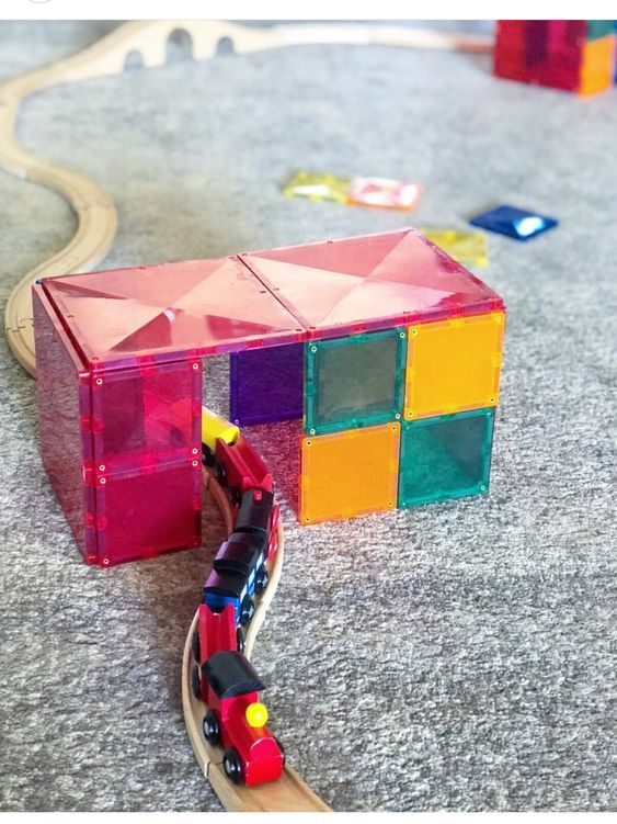 a toy train is on the tracks near a colorful cube structure that looks like a house