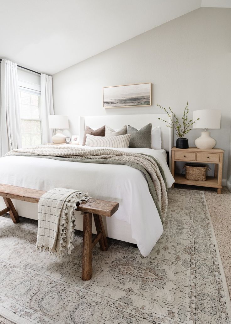 a bedroom with a large bed and wooden bench in front of the window, along with two lamps on either side of the bed