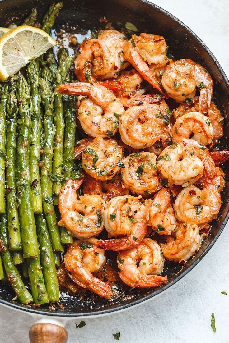 shrimp and asparagus in a skillet with lemon wedges on the side