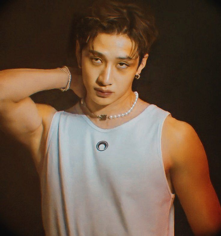 a young man wearing a white tank top and pearl necklace